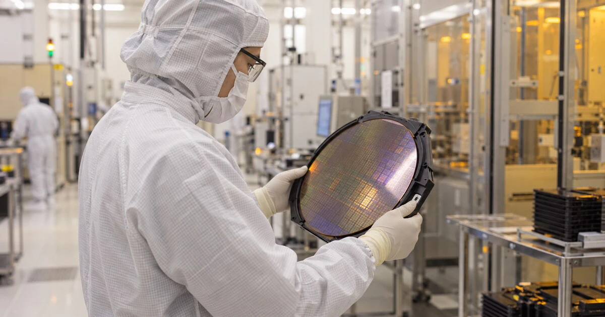 A cleanroom engineer examines a silicon wafer inside a semiconductor fabrication facility.